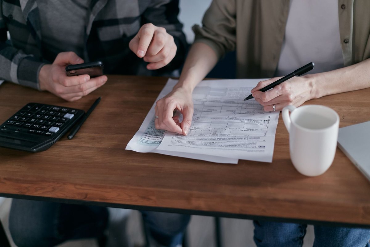 Two people at a wooden table reviewing a printed loan document with a pen, a calculator, and a smartphone