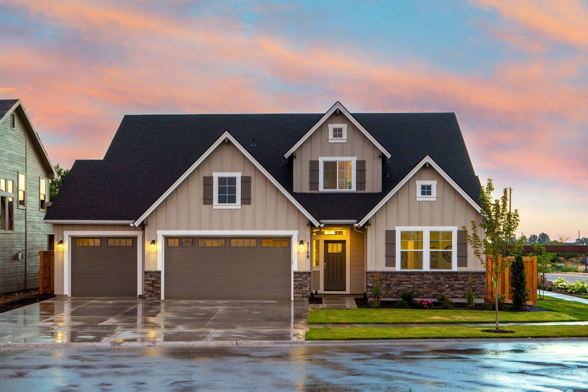 Gray craftsman-style single-family home with a two-car garage, stone accents, and a wet driveway at dusk