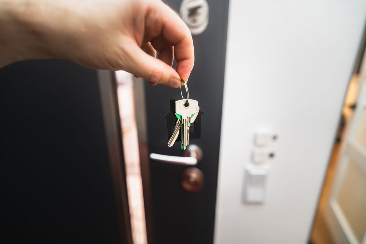 Hand holding a set of house keys in front of an open front door