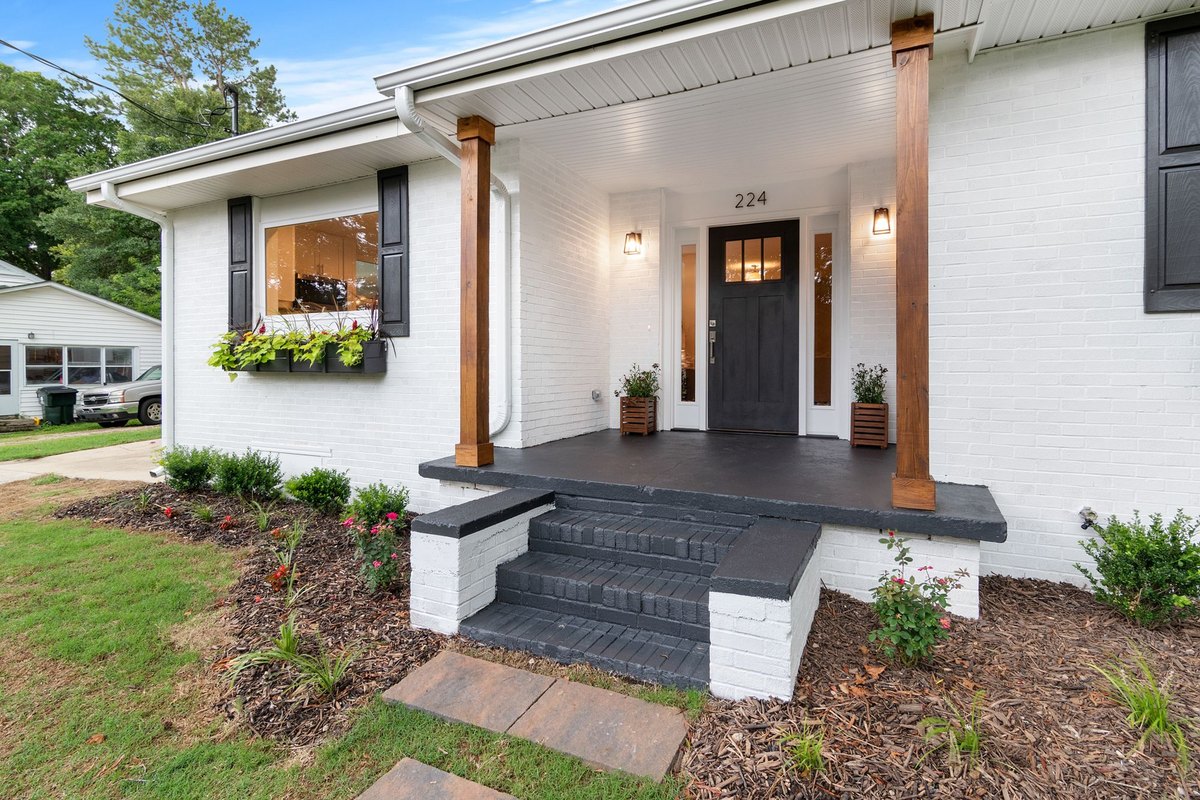White single-story starter home with a covered front porch, dark front door, and a small landscaped front yard