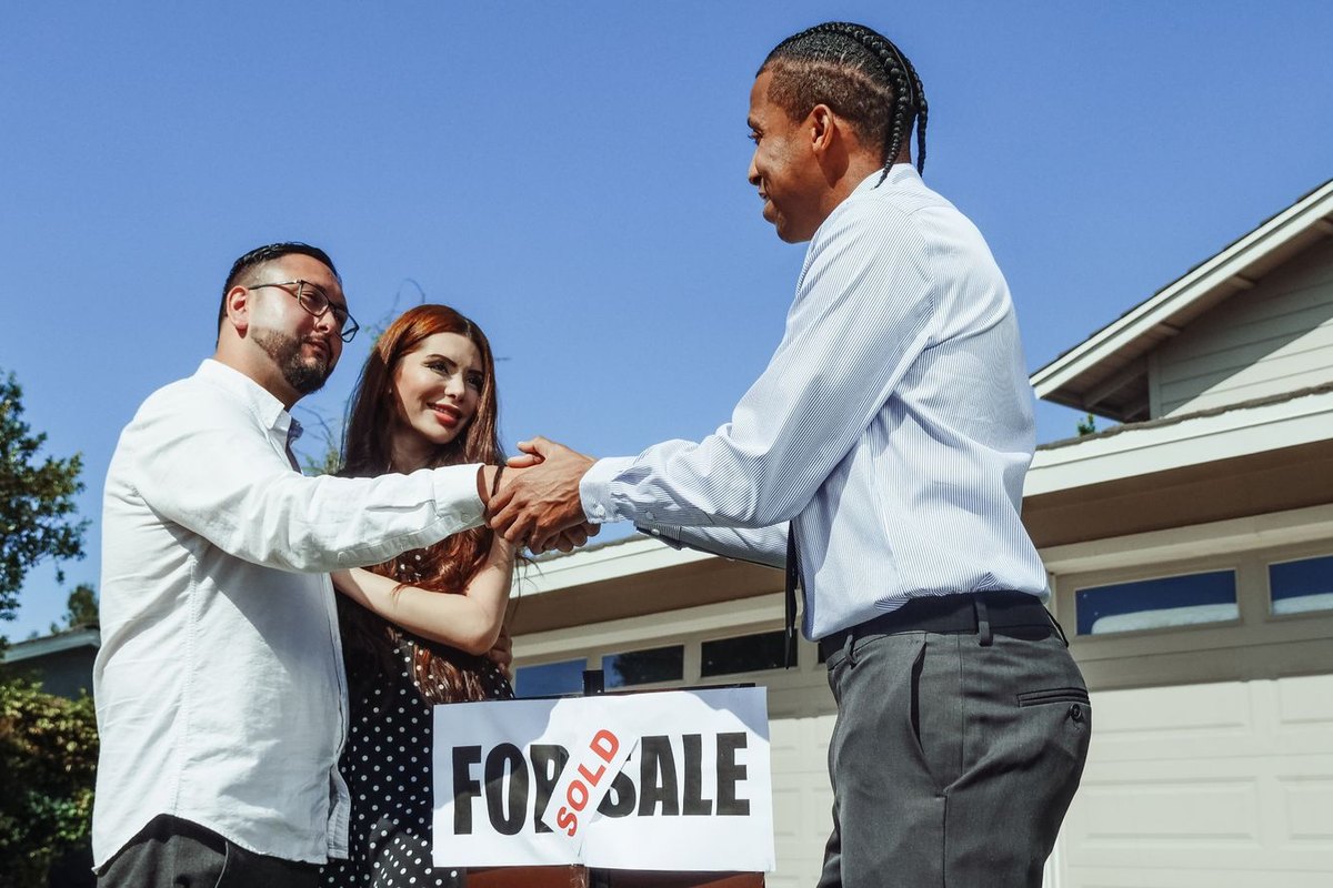 Couple shaking hands with their real estate agent next to a sold sign in front of a house with a white garage