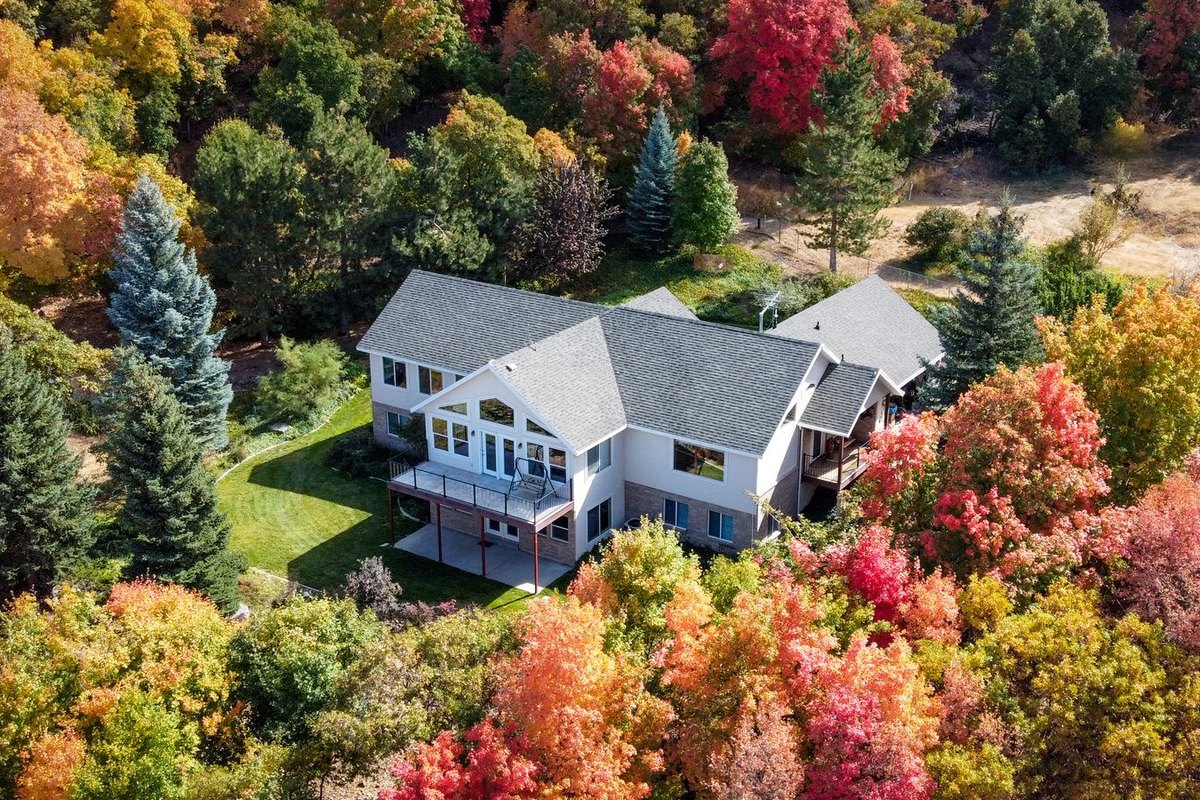 Aerial view of a two-story white house with a gray roof surrounded by autumn trees in red, orange, and green