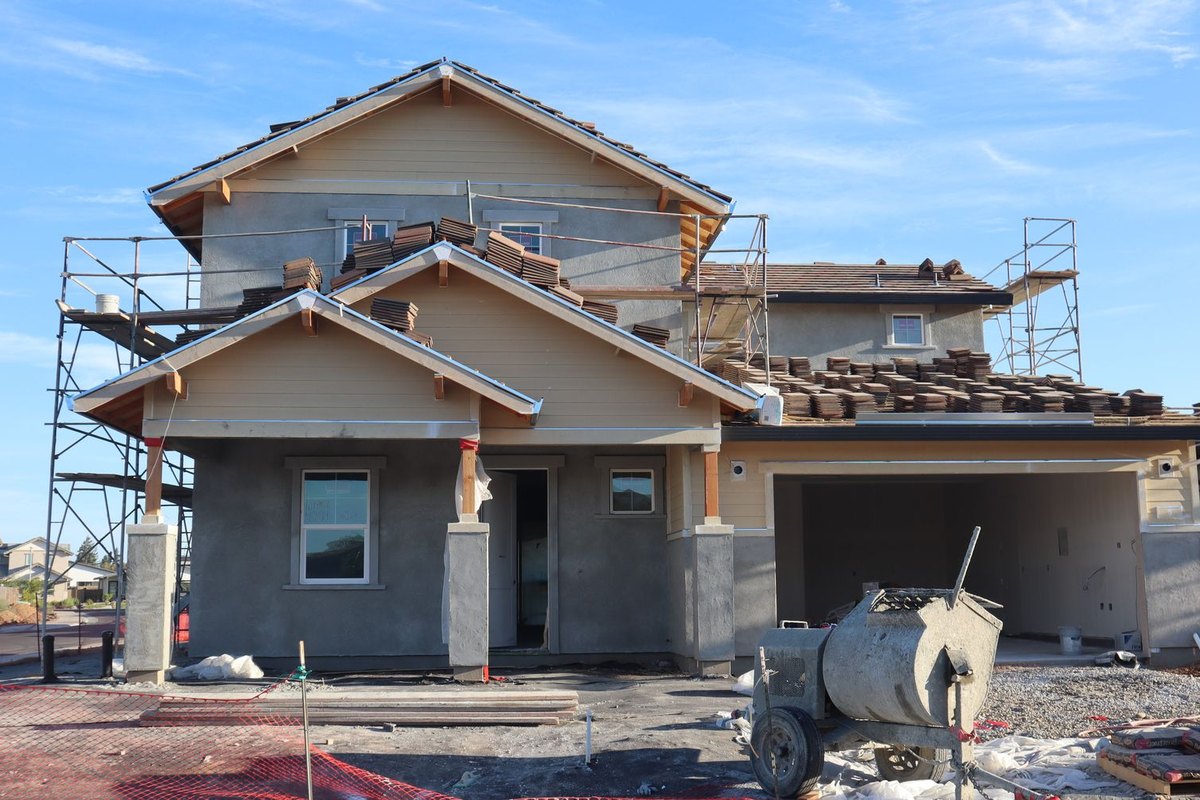 Two-story suburban home under construction with scaffolding, fresh siding, and a dirt front yard waiting for landscaping