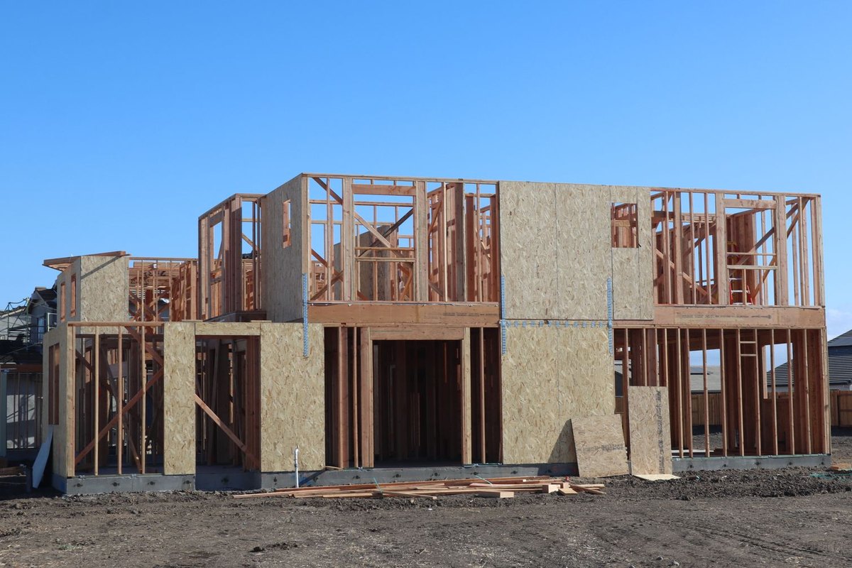 Wood-framed new homes under construction on a suburban street with blue sky, a common sight in fast-growing Treasure Valley subdivisions