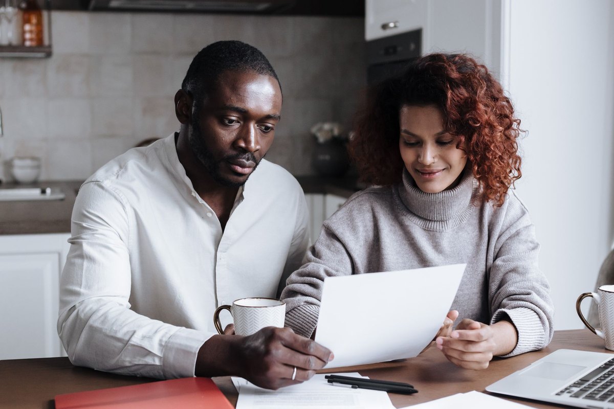 Couple sitting at a kitchen table reviewing loan documents together with coffee mugs and a laptop