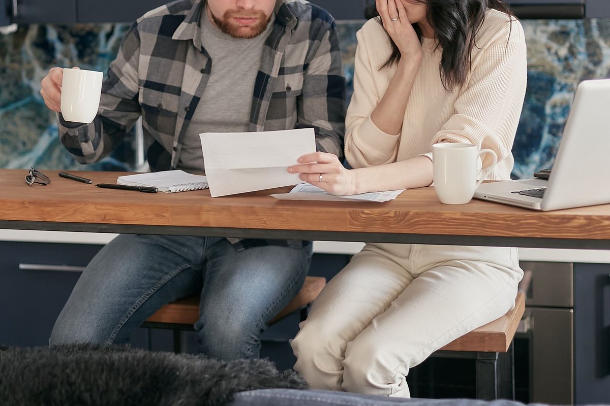 Couple at a kitchen table looking surprised while reviewing a document and bills