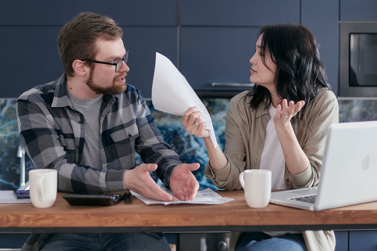 Couple at a kitchen table reviewing loan papers and a laptop while discussing their monthly budget