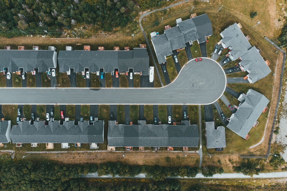 Aerial view of a new suburban subdivision with rows of townhomes around a cul-de-sac and undeveloped land nearby