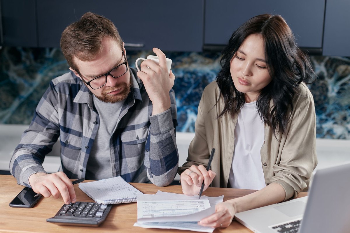 Couple sitting at a kitchen table with a laptop, a calculator, and a stack of bills, reviewing their monthly budget together