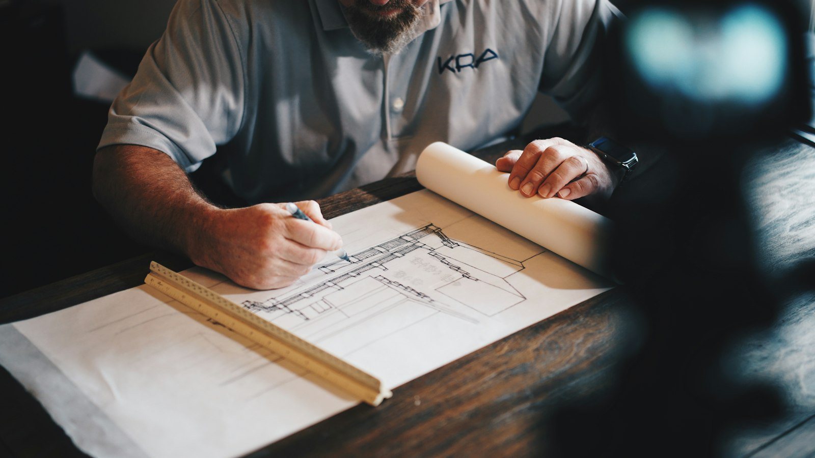 Person reviewing architectural blueprints on a wooden table with a pencil