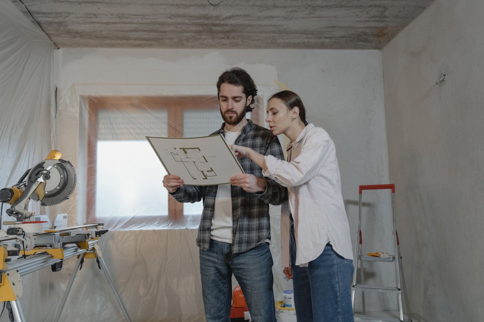 Couple reviewing blueprints inside a home under renovation