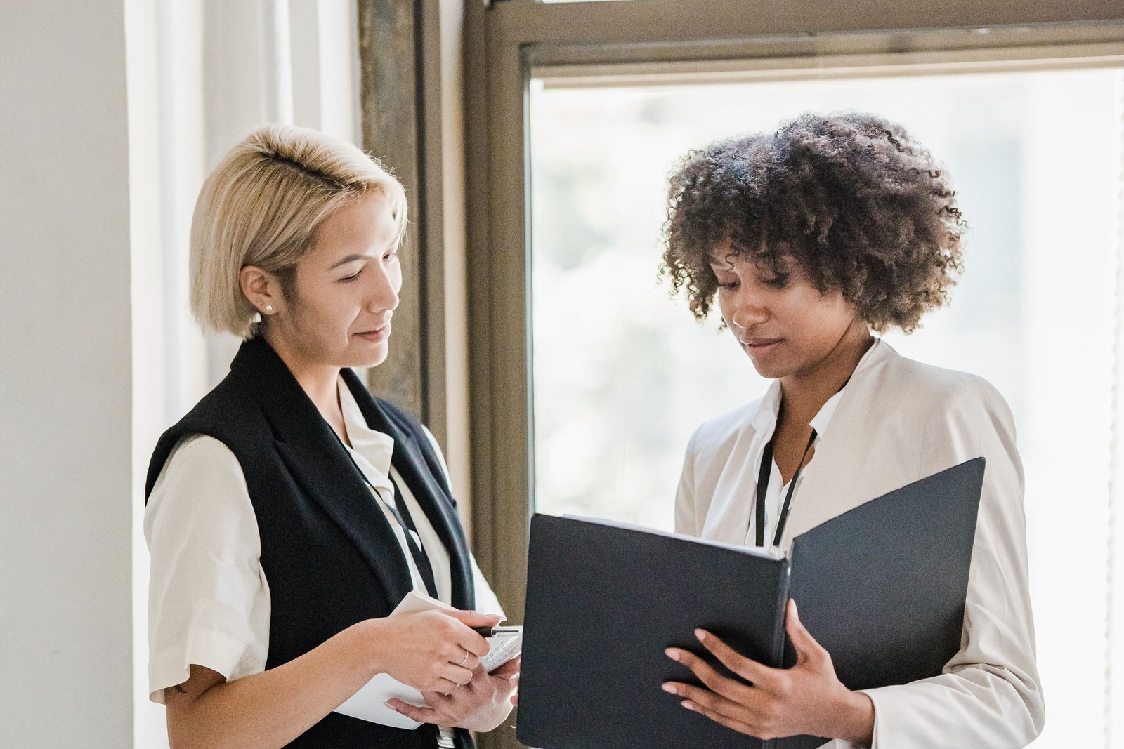 Two professionals reviewing a document folder near a large office window