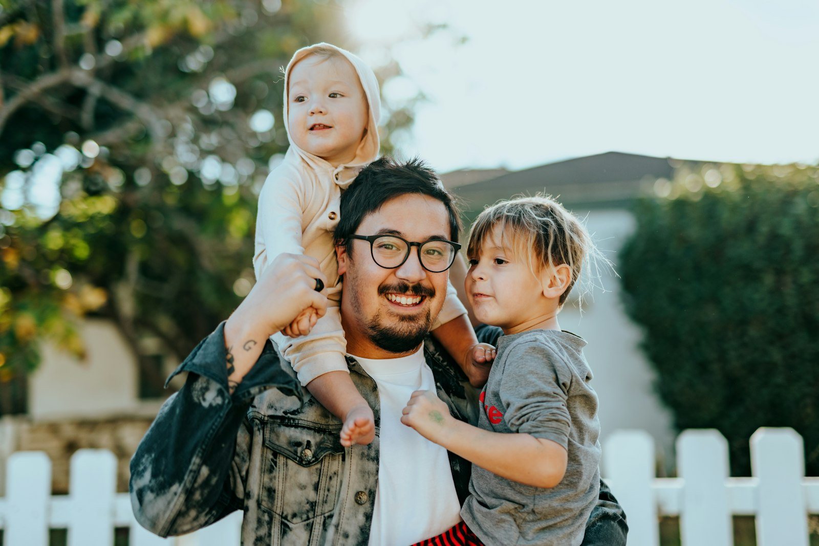Parent outdoors holding two young children and smiling