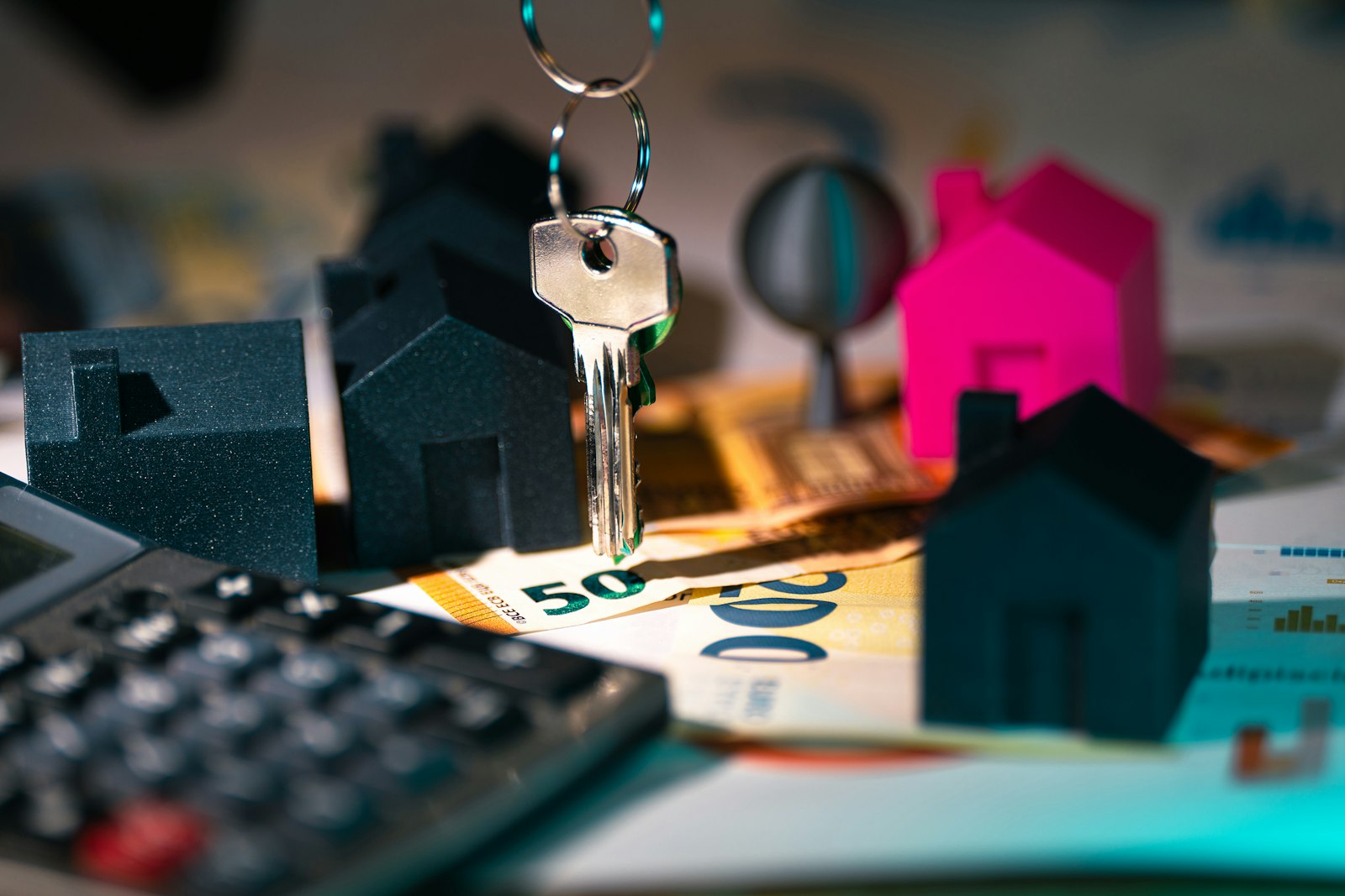 House key hanging above miniature homes and a calculator on a desk, illustrating mortgage payment math