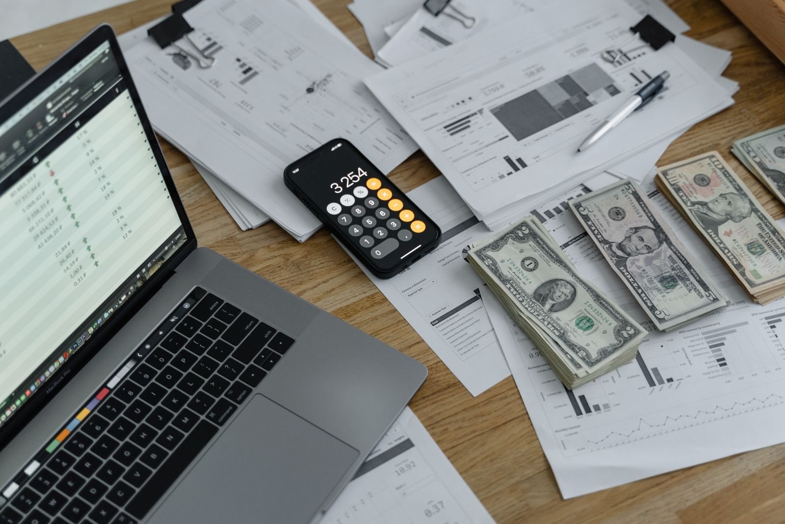 Laptop, calculator, cash, and paperwork spread across a desk