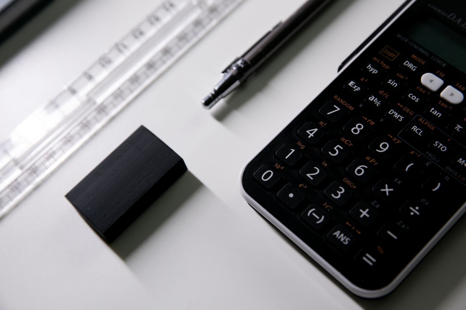 Calculator, pen, ruler, and eraser on a white desk