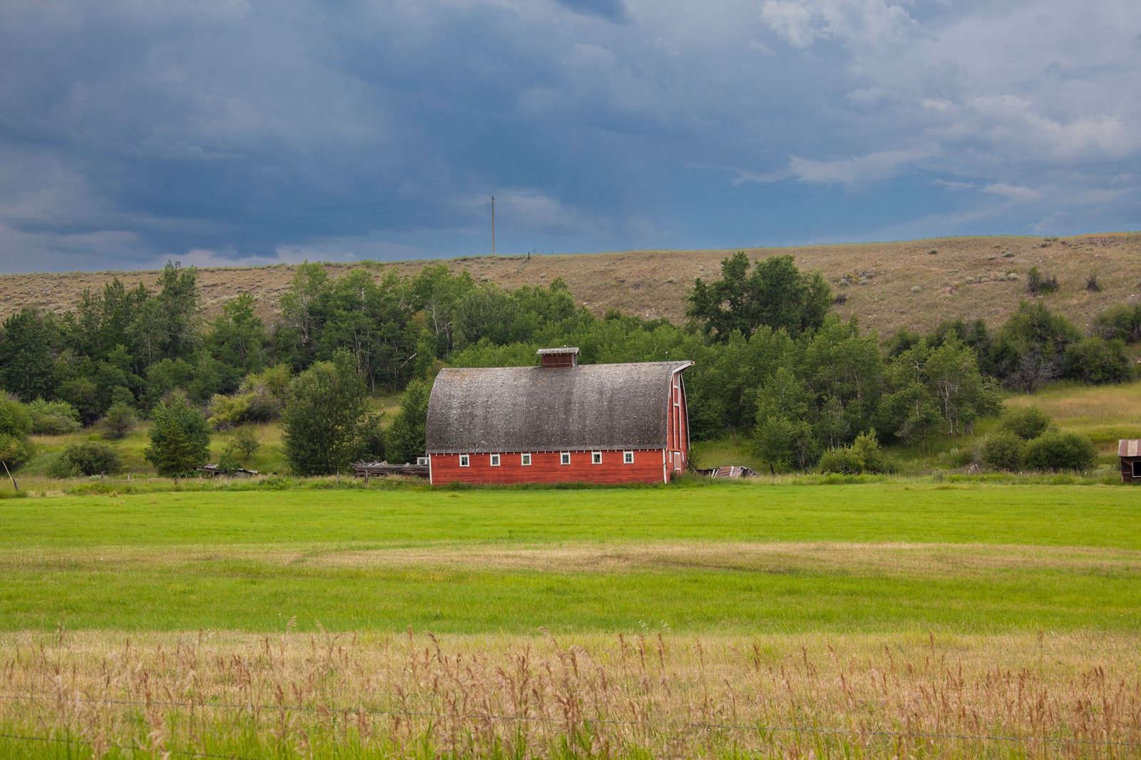 Red barn in a wide green field under a blue sky