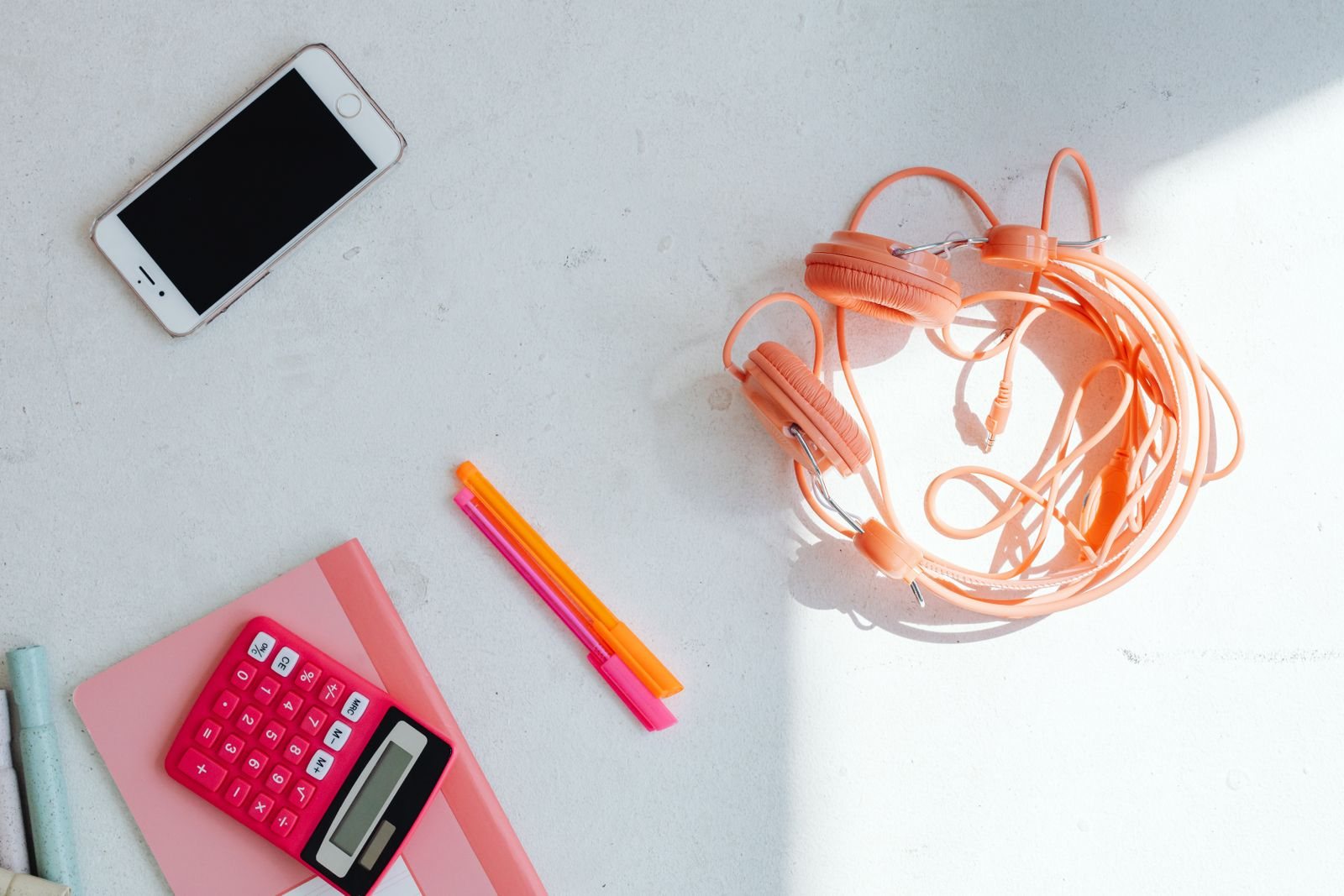Pink calculator, phone, earbuds, and highlighters on a white desk