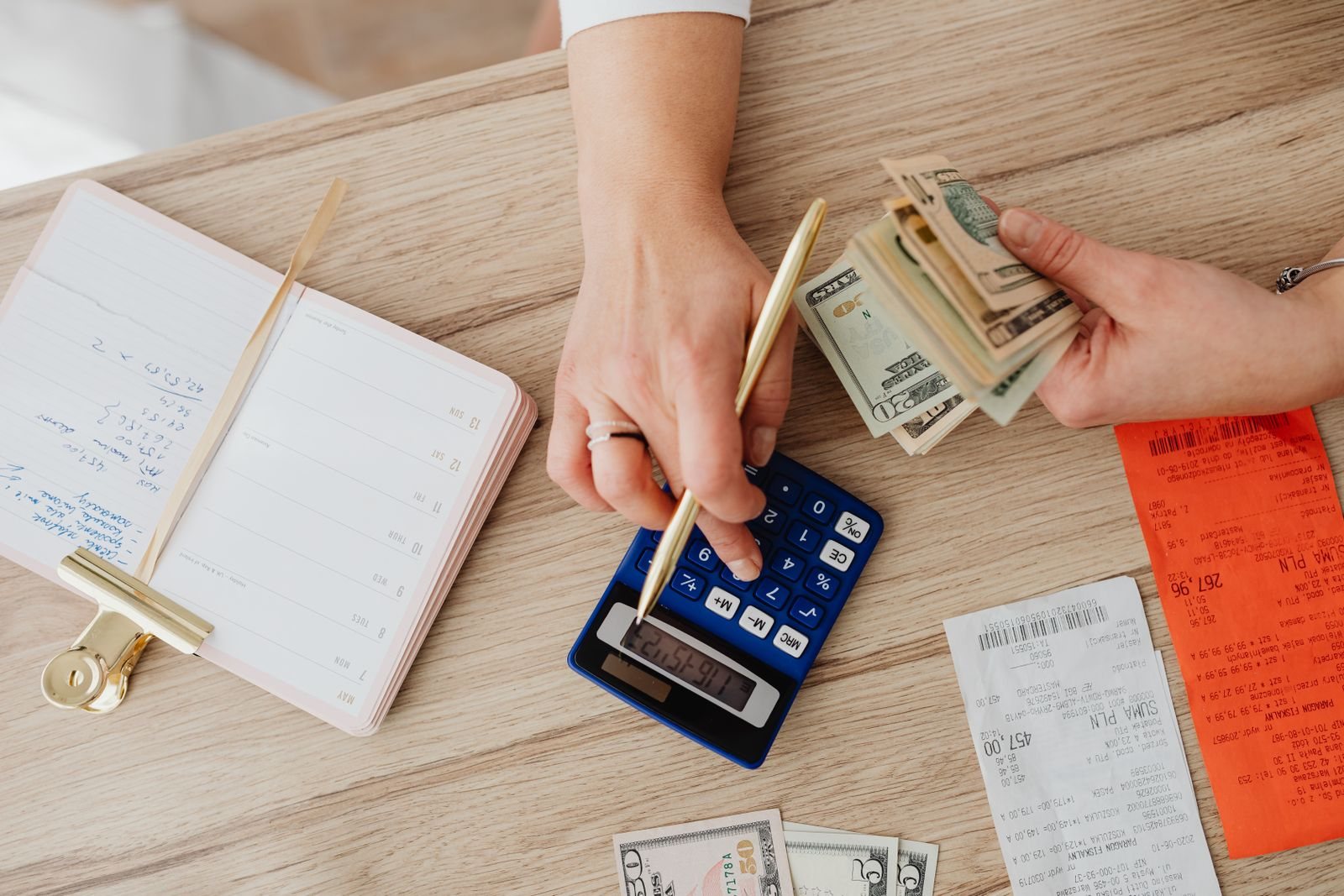 Hands counting cash next to a calculator and a notebook