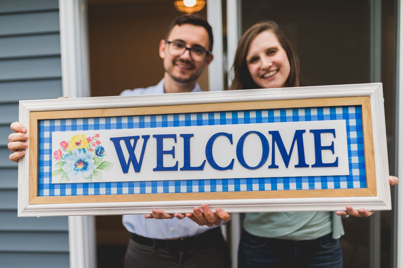 Couple holding a welcome sign at the front door of their home